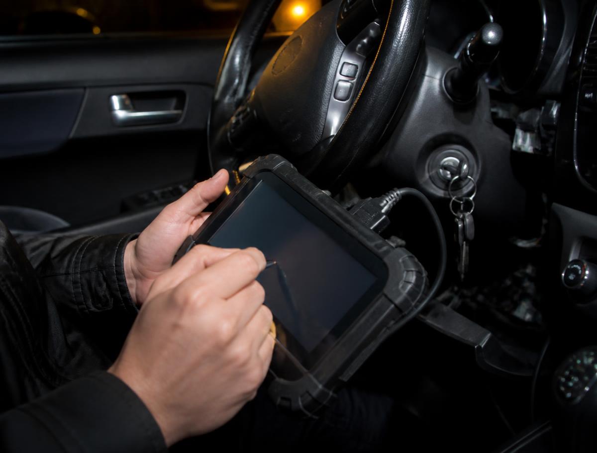 Locksmith using a diagnostic programming tablet beside a car ignition barrel